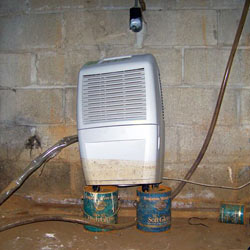 A crawl space dehumidifier up on coffee cans, with a muddy water mark halfway up the system.